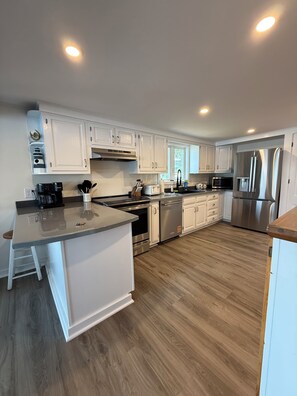 A modern kitchen with white cabinetry, stainless steel appliances, and a wooden floor. - Heron's Landing (Harpswell)