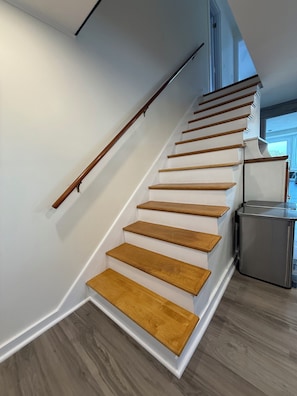 Una escalera de madera con barandilla de metal que conduce a una cocina con refrigerador de acero inoxidable.