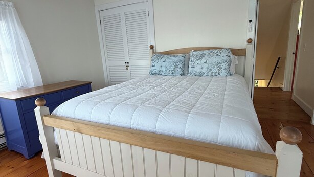 A bedroom with a wooden bed frame, a blue dresser, and a white door. - Heron's Landing (Harpswell)