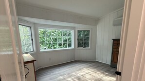 A spacious room with large windows, a wooden floor, and a ceiling light fixture. - Heron's Landing (Harpswell)