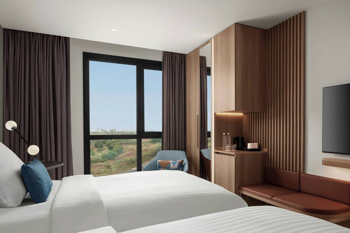 A modern hotel room with a large bed, a seating area, a desk, and a TV.