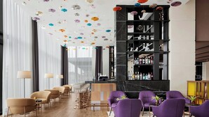 Ein moderner Barbereich mit einer langen Theke, Barhocker und einer Sitzgruppe mit violetten Stühlen.