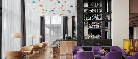 Una zona de bar moderna con una barra alargada, taburetes y un espacio de estar con sillas moradas.