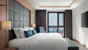Ein modernes Hotelzimmer mit einem großen Bett, einer Sitzecke und Blick auf die Stadt durch das Fenster.