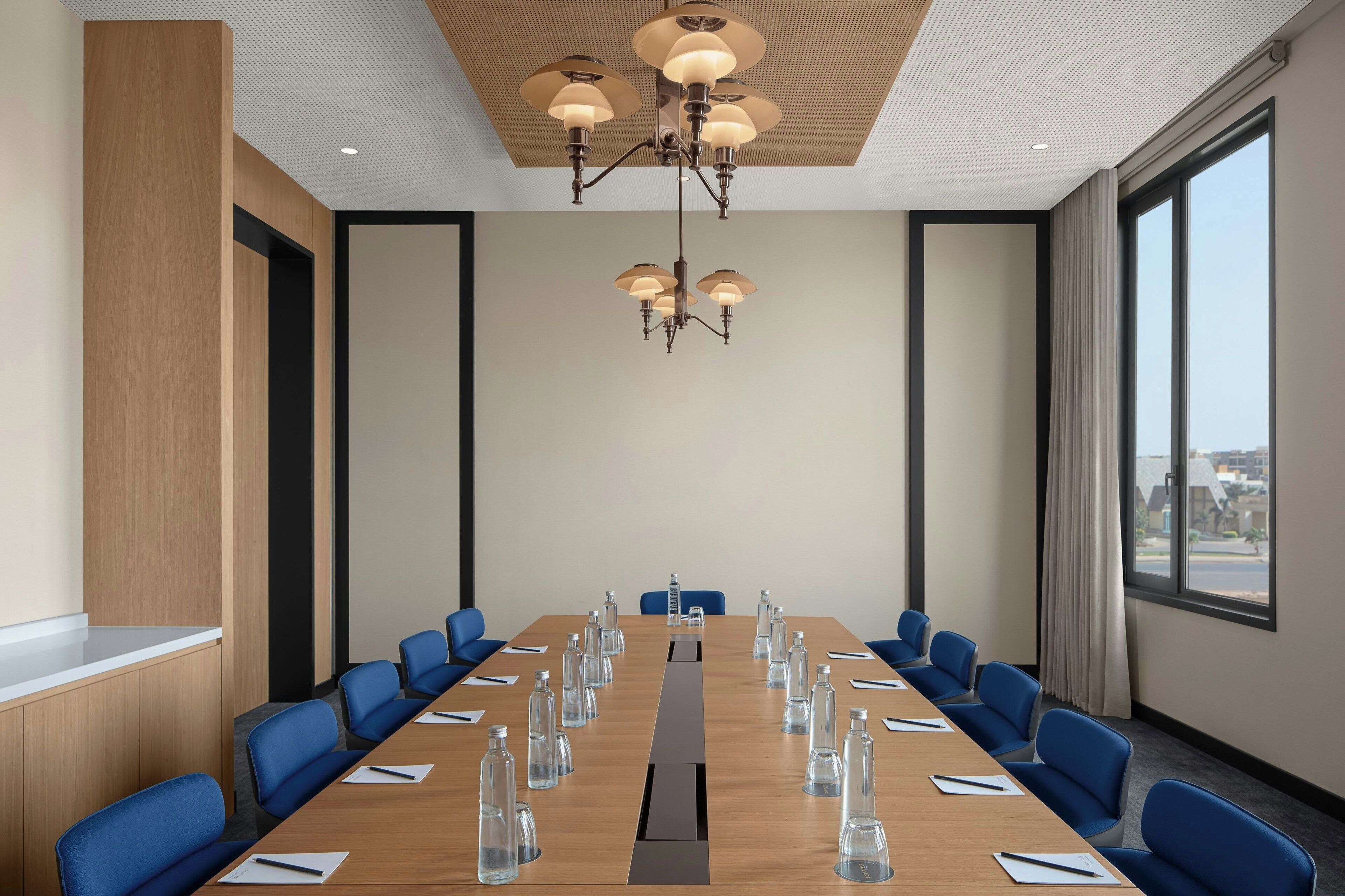 Une salle de conférence avec une longue table, des chaises bleues et un lustre.