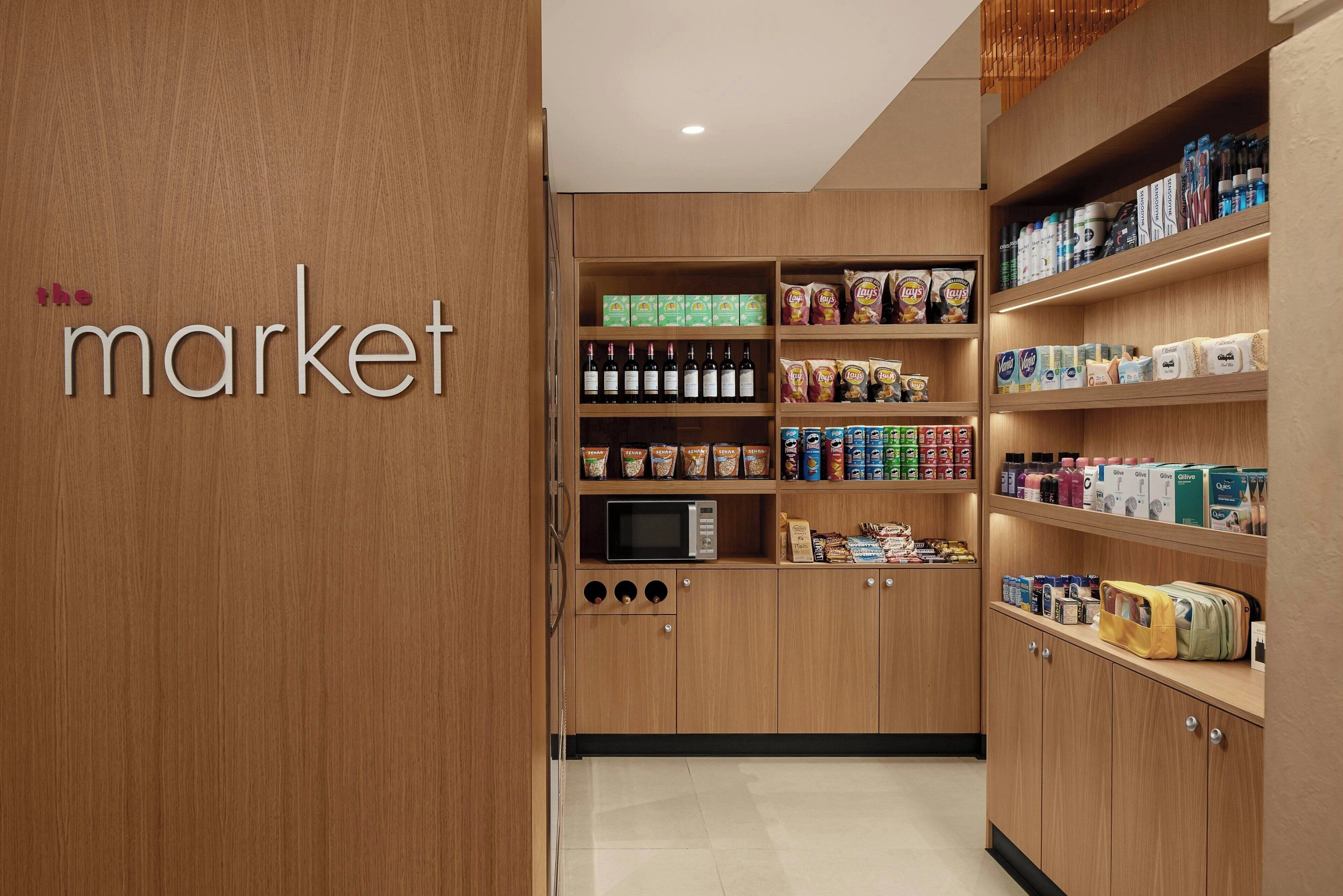 A wooden interior with a 'market' sign, shelves stocked with snacks, beverages, and packaged goods.