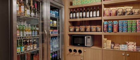 A kitchenette with a refrigerator stocked with beverages, a microwave, and shelves with snacks and condiments.