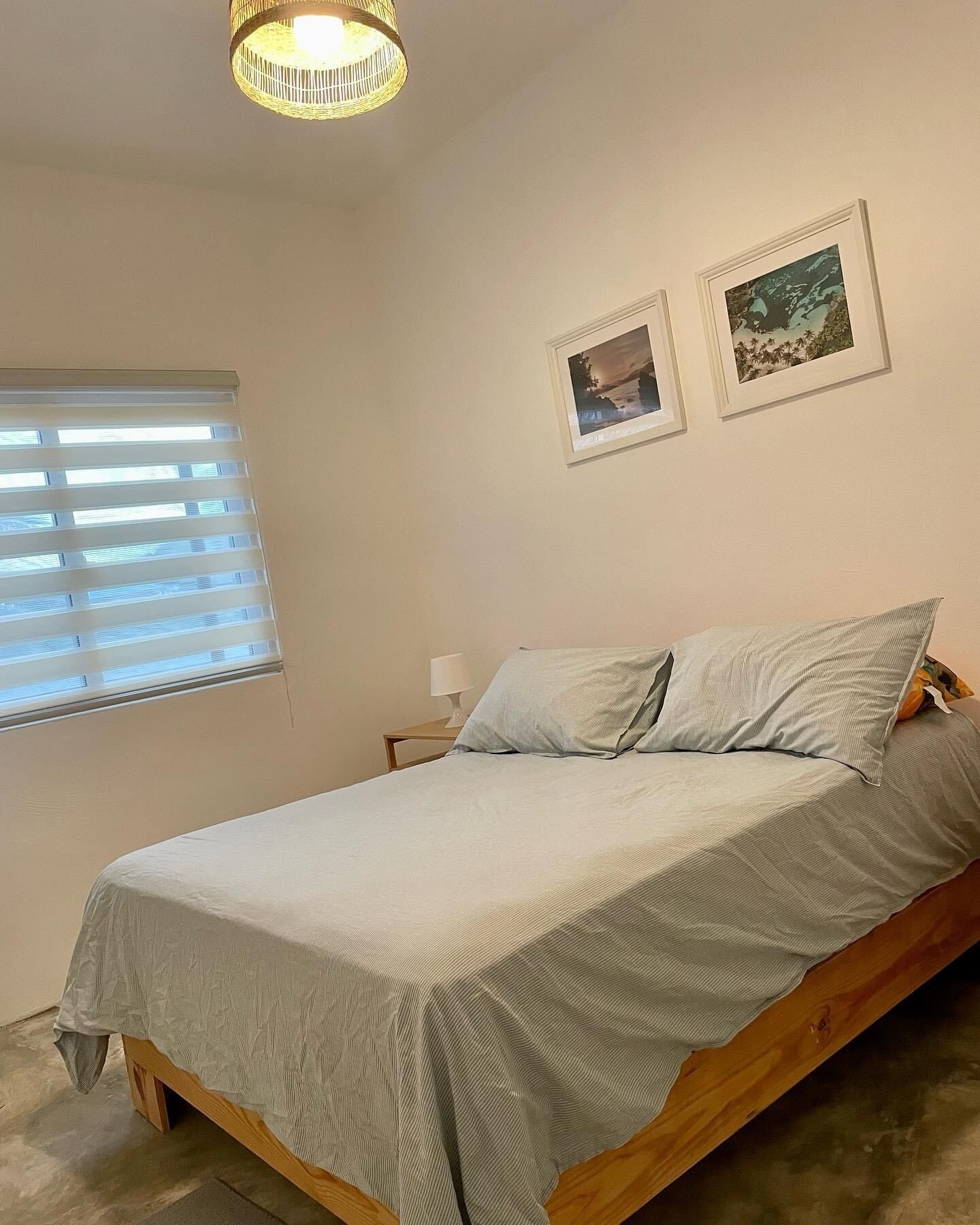 Un dormitorio con una cama, una mesita de noche, una lámpara y dos cuadros en la pared.