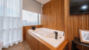 Une salle de bain moderne avec un meuble-lavabo en bois, une grande baignoire et une vue sur la ville grâce à de grandes fenêtres.