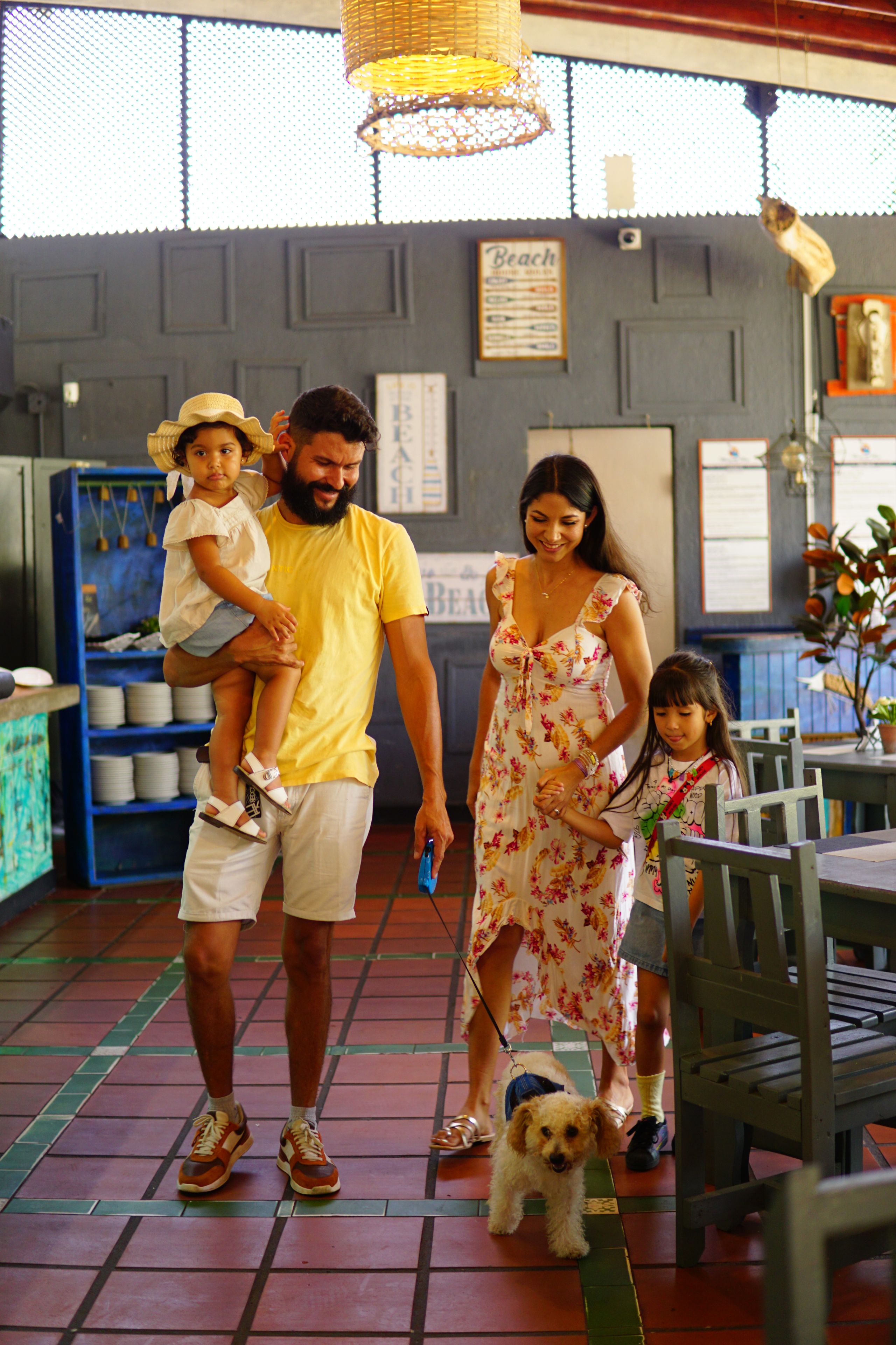 A family with a child and a dog inside a restaurant with tiled floors and a blue wall.