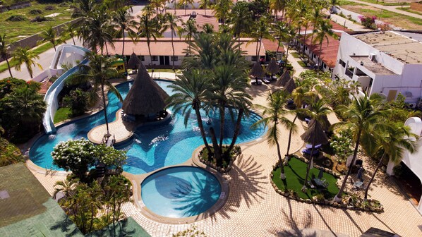 Un resort con una gran piscina, palmeras y una estructura de techo de paja.