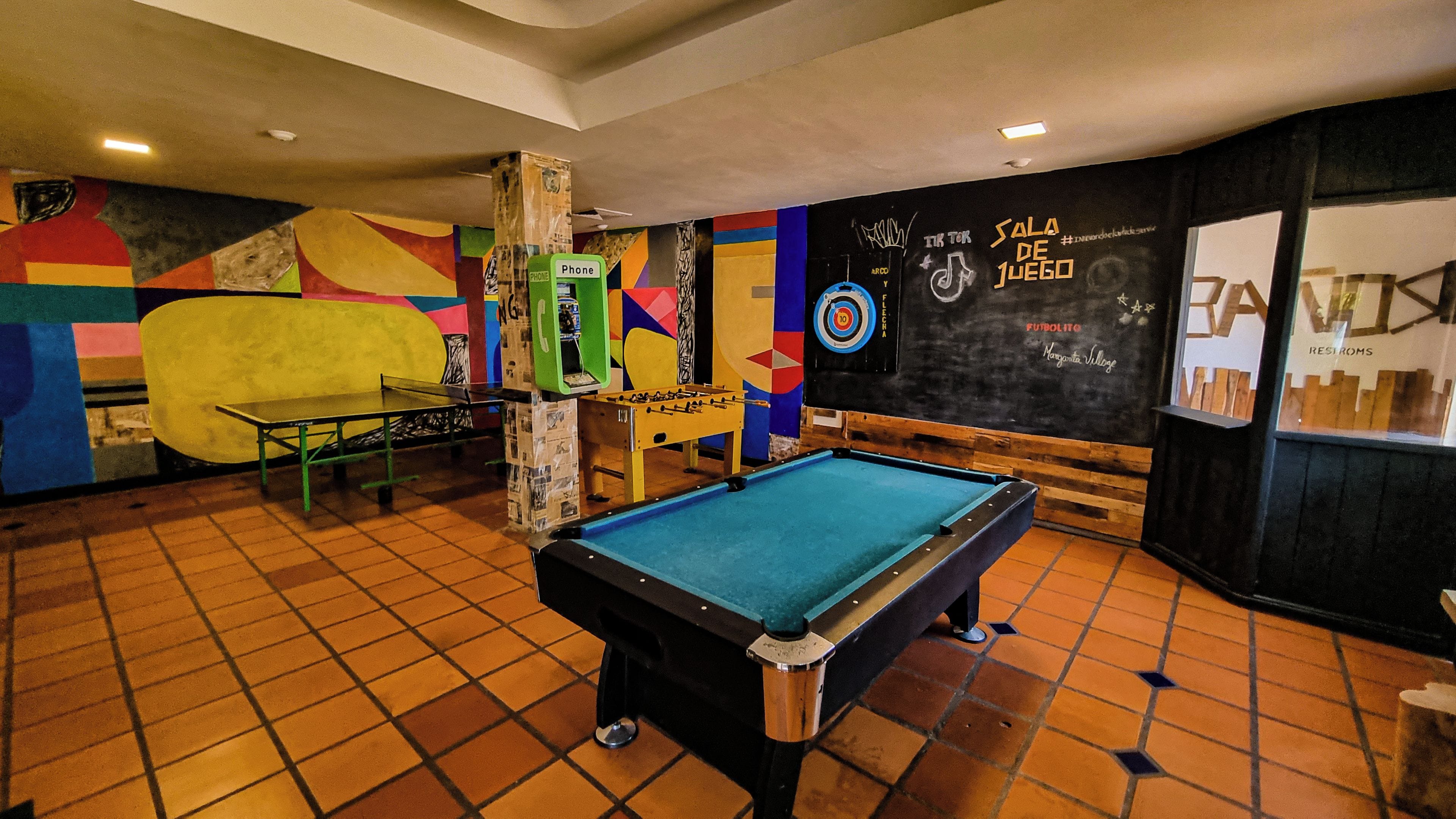 Mesa de bilhar em um espaço com um mural colorido, mesa de futebol de mesa e alvo de dardos.