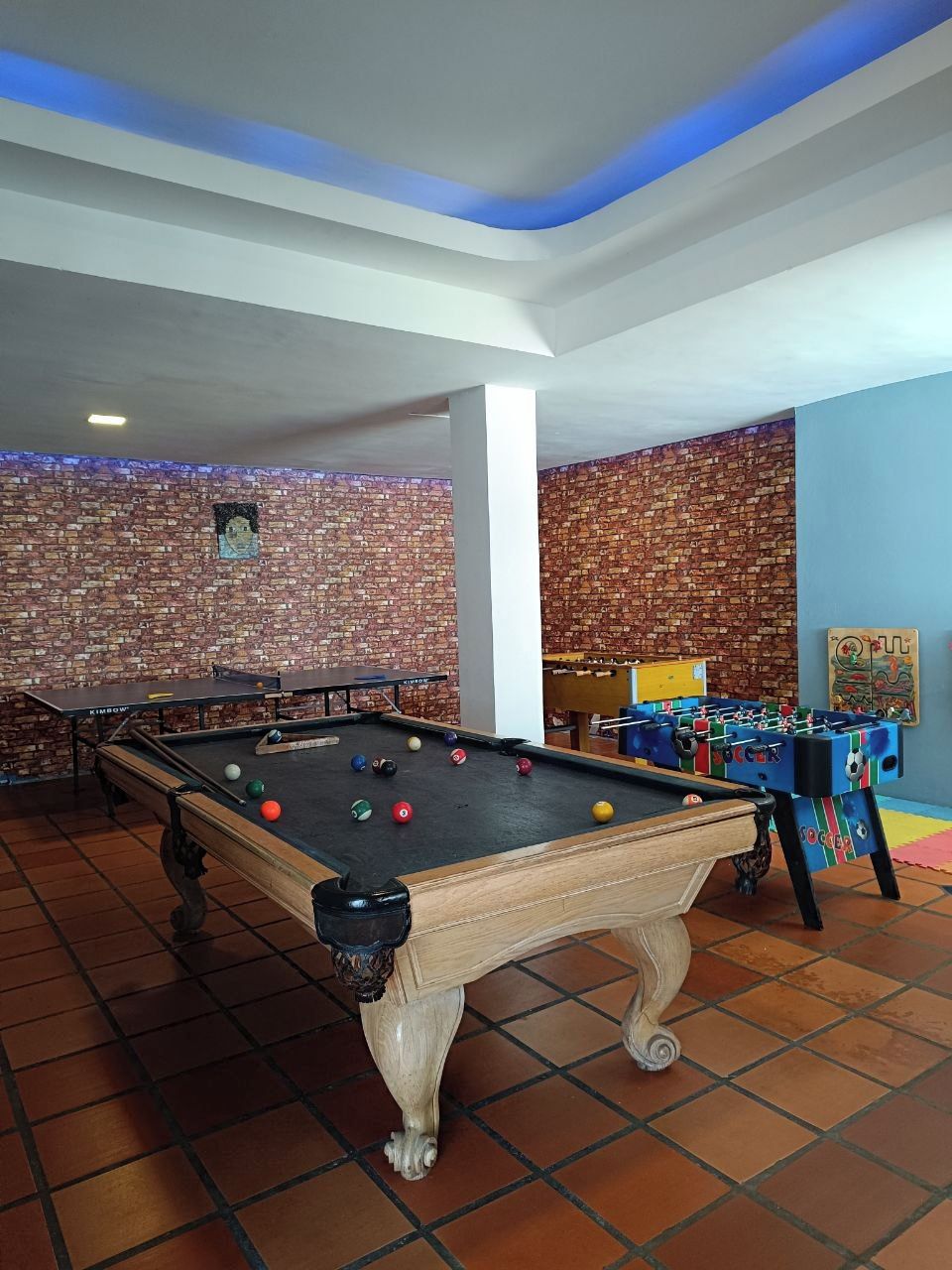 A pool table with balls, a foosball table, and a brick wall.