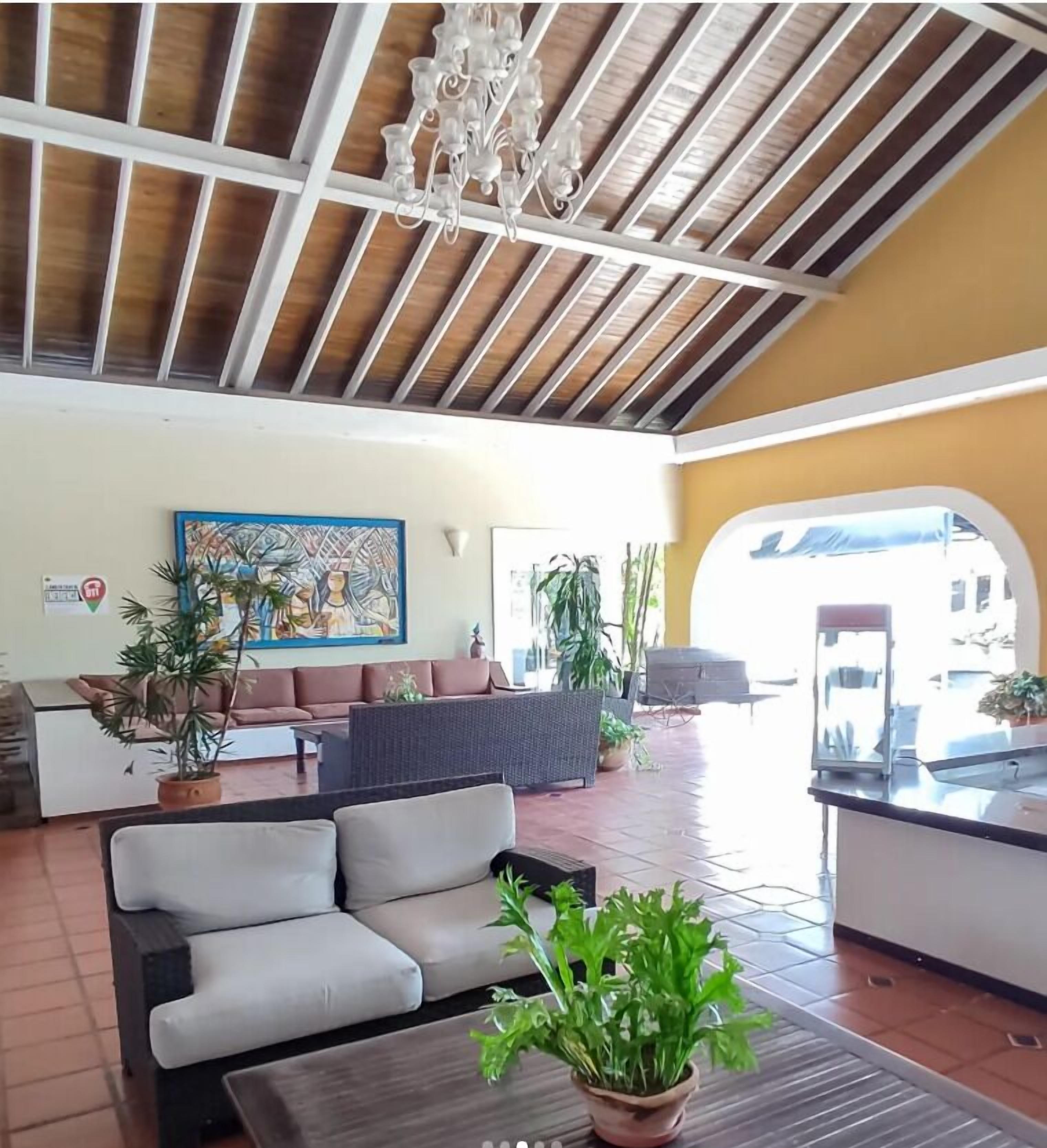A spacious lobby with a high ceiling, a chandelier, a sofa, a dining area, and potted plants.