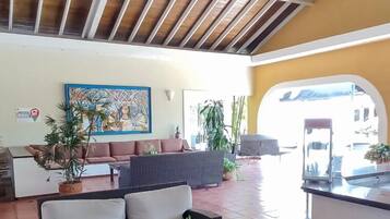 A spacious lobby with a high ceiling, a chandelier, a sofa, a dining area, and potted plants.