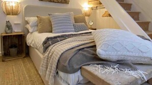 Une chambre confortable avec un lit, un banc en bois, un escalier et un miroir au mur.