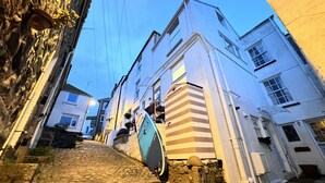 Une ruelle pavée bordée de bâtiments historiques, avec une planche de surf appuyée contre l’un d’eux.