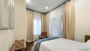 Ett hotellrum med en säng, en stol och ett fönster med gardiner.