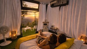 Ein Schlafzimmer mit Bett, Ventilator, Lampe und Blick auf eine Landschaft.