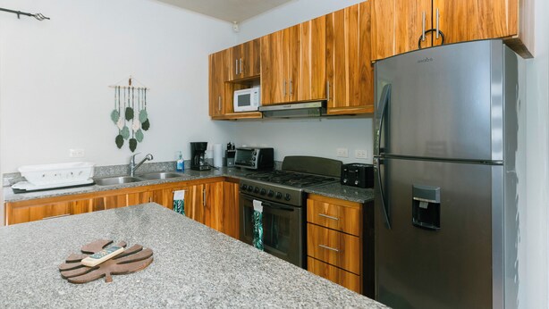Una cocina con armarios de madera, un refrigerador de acero inoxidable, un microondas, una estufa y una encimera de granito.