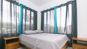 Un dormitorio con cama, dos mesitas de noche, cortinas de gasa y vistas a árboles.