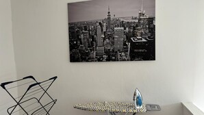 A room with a cityscape painting, a metal drying rack, and an ironing board with an iron. - Cozy Coastal Getaway in North Shields (North Shields)