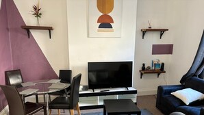 A modern living room with a flat-screen TV, a glass coffee table, a sofa, and a dining area with chairs. - Cozy Coastal Getaway in North Shields (North Shields)