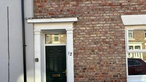 A brick building with a black door and a white window frame. - Cozy Coastal Getaway in North Shields (North Shields)