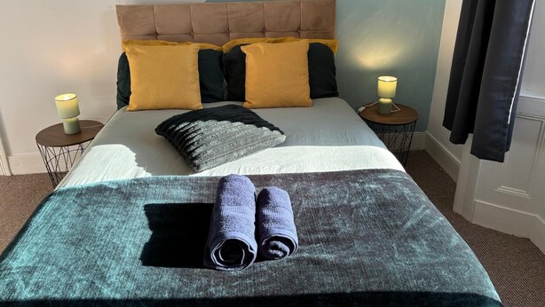 A neatly made bed with a headboard, two bedside tables with lamps, and a pair of rolled towels on the bed. - Cozy Coastal Getaway in North Shields (North Shields)