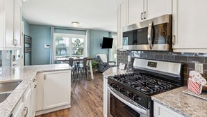 Una cocina moderna con armarios blancos, un microondas de acero inoxidable, una estufa a gas y un comedor con mesa y sillas.