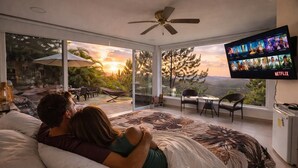 Quarto com cama grande, televisão na parede e vista para o exterior.