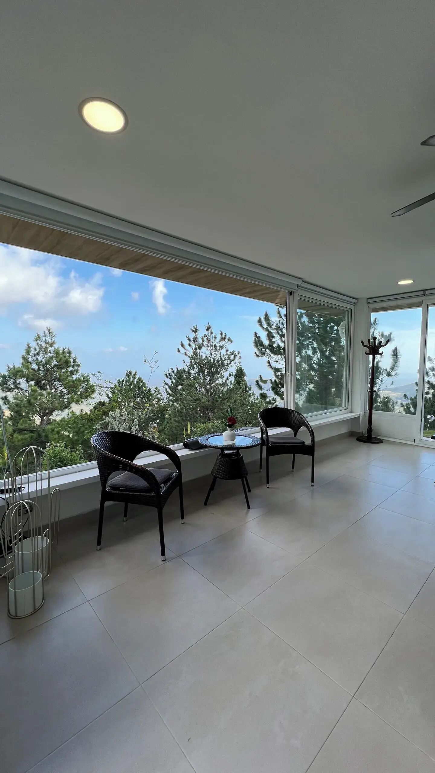 Un balcon spacieux offrant une vue sur les arbres et un ciel dégagé. On y trouve deux fauteuils en osier noir et une petite table ronde sur laquelle est posé un vase.