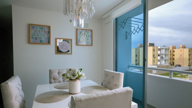 En matplats med ett vitt bord, bekväma stolar, en vas med blommor och inramade konstverk på väggen.