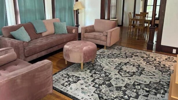 Een woonkamer met een bruine bank, een roze fauteuil en een vloerkleed met dessin.