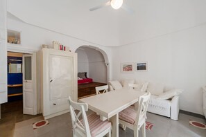 A room with a white dining table, white chairs, a white sofa, a white cabinet, and a ceiling fan.
