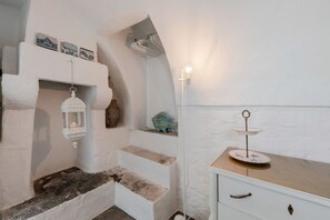 A room with white walls, a stone fireplace, a white dresser, and a small shelf with decorative items.