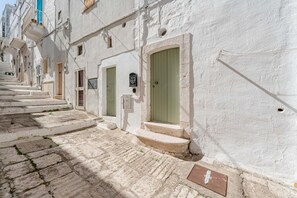 A narrow street with white buildings, green doors, and stone steps.