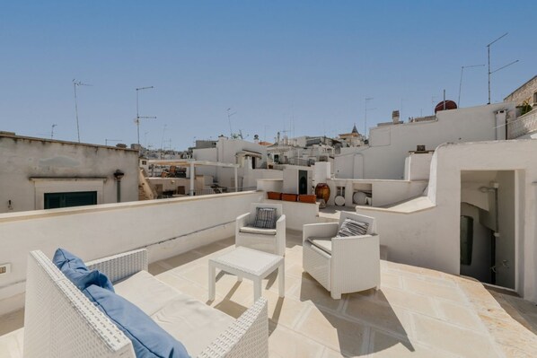 A rooftop terrace with white wicker furniture, a small table, and a sofa.