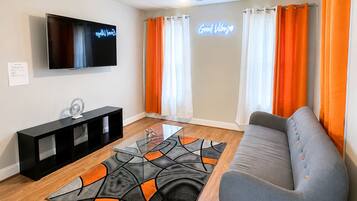 A living room with a flat-screen TV, a sofa, a coffee table, and a patterned rug.