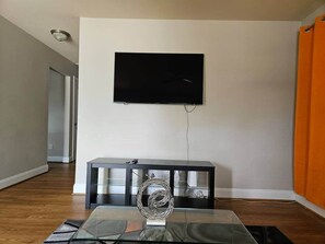 A living room with a flat-screen TV mounted on the wall, a glass coffee table with a metallic sculpture, and a black entertainment unit. - Private Villa 3-Bed|  7 min from Downtown (Raleigh)