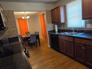 A modern kitchen with dark wooden cabinets, a granite countertop, and a dining area with a table and chairs. - Private Villa 3-Bed| 7 min from Downtown (Raleigh)