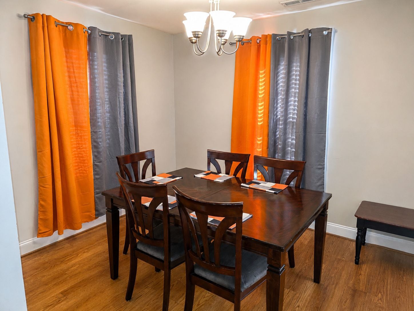 A dining area with a wooden table and chairs, orange and gray curtains, and a chandelier.