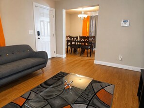 A living room with a sofa, a glass coffee table, and a dining area with chairs and a chandelier.