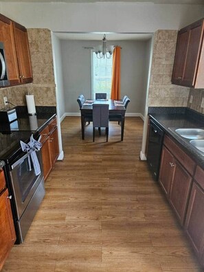 A kitchen with wooden cabinets, a dining table with chairs, and a window with curtains. - Private Villa 3-Bed| 7 min from Downtown (Raleigh)