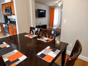 A dining area with a dark wooden table, two chairs, and a television mounted on the wall.
