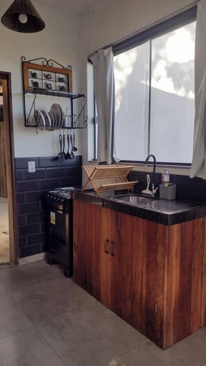 Una cocina con mostrador de madera, estufa a gas, pileta y ventana con cortinas.