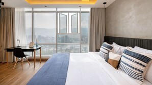A modern hotel room with a large bed, a desk, and a view of the city through large windows. - Impressive 2BR apt with Jacuzzi & A/C in El Poblado (Medellín)