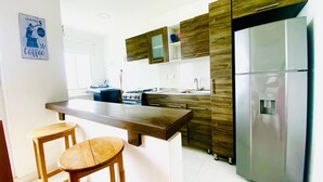 A modern kitchen with a central island, wooden stools, a stainless steel refrigerator, and wooden cabinets. - Family apartment, Coveñas, Caribe Campestre (Coveñas)