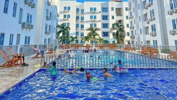 A swimming pool surrounded by white buildings with multiple floors and balconies, under a clear blue sky. - Family apartment, Coveñas, Caribe Campestre (Coveñas)