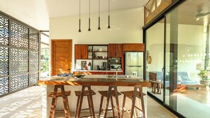 A modern kitchen with a central island, bar stools, wooden cabinets, and a large window.